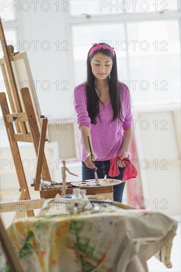 Mixed race teenage girl painting in studio