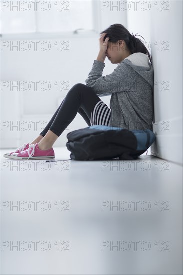 Mixed race teenage girl covering her face in school hallway