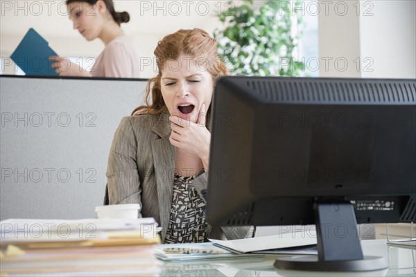 Caucasian businesswoman yawning at desk