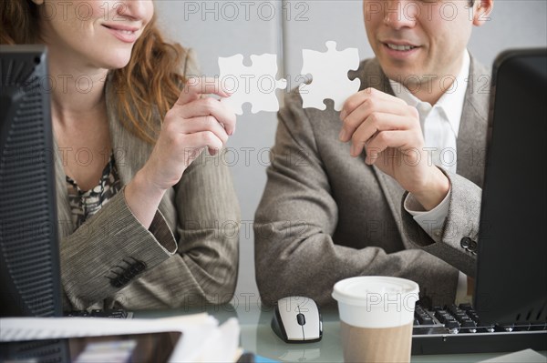 Business people putting puzzle pieces together at desk