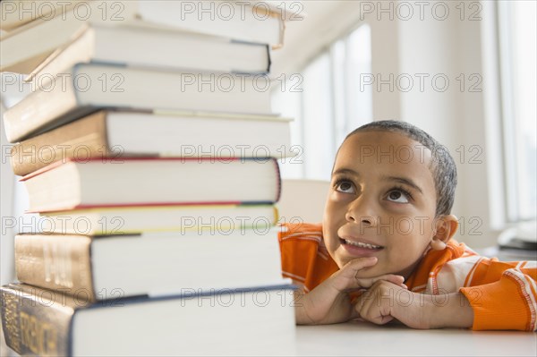 Mixed race boy looking up at stack of books