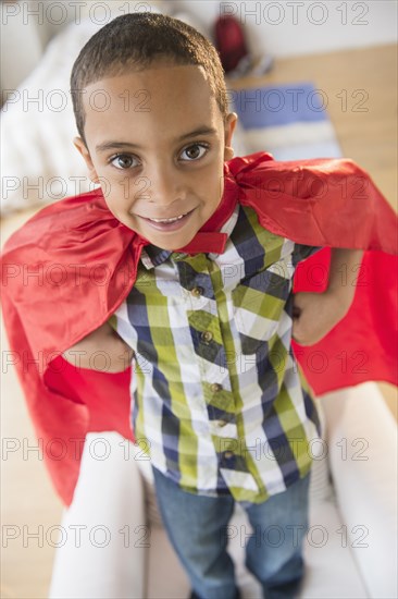 Mixed race boy wearing cape on armchair