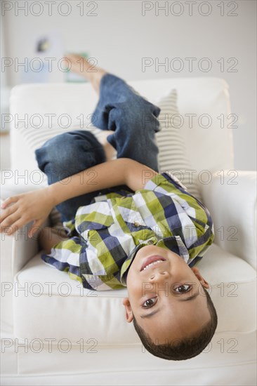 Mixed race boy laying upside-down on armchair