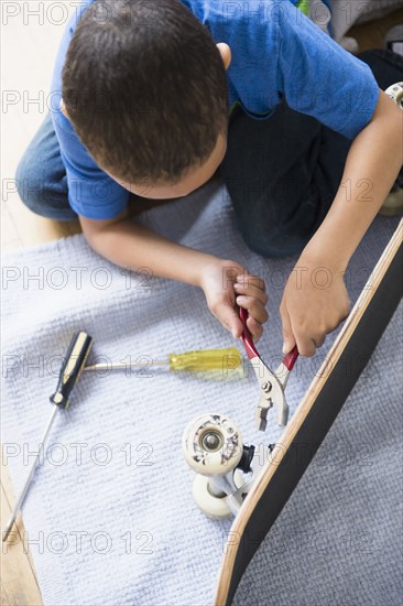 Mixed race boy fixing skateboard