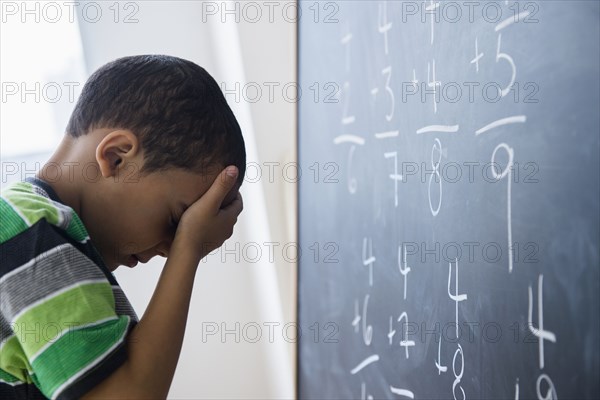 Mixed race boy doing math problems at board in class