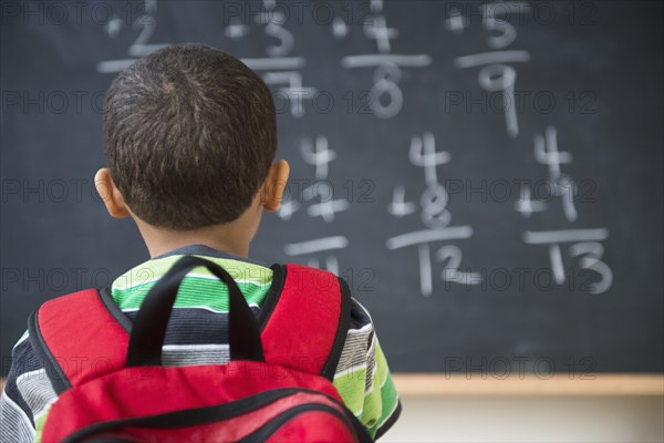 Mixed race boy doing math problems at board in class