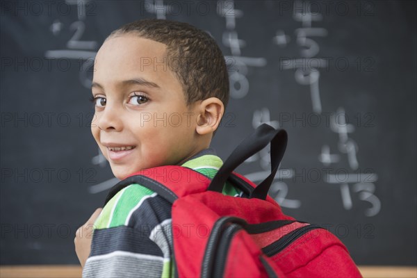 Mixed race boy doing math problems at board in class