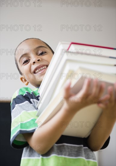 Mixed race boy carrying stack of books in class