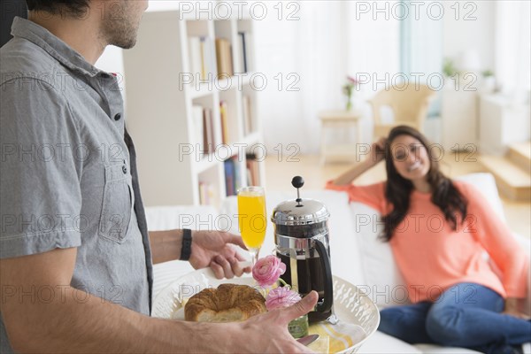 Man serving girlfriend breakfast on sofa