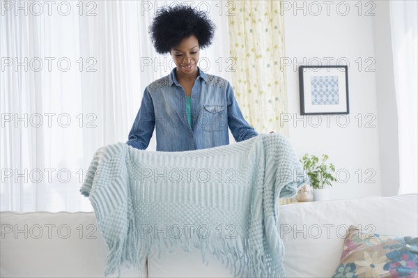 African American woman folding blanket on sofa