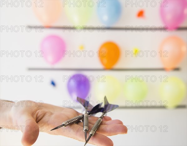 African American woman holding darts by wall of balloons