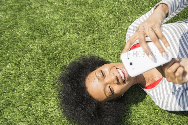 African American woman laying in grass using cell phone