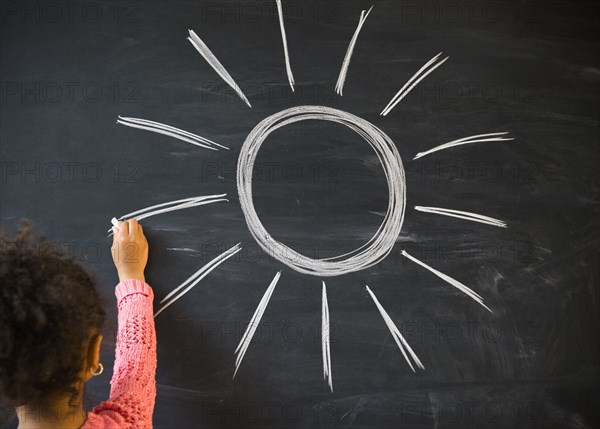 African American girl drawing sun on board in classroom