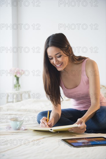 Woman taking notes with tablet computer on bed