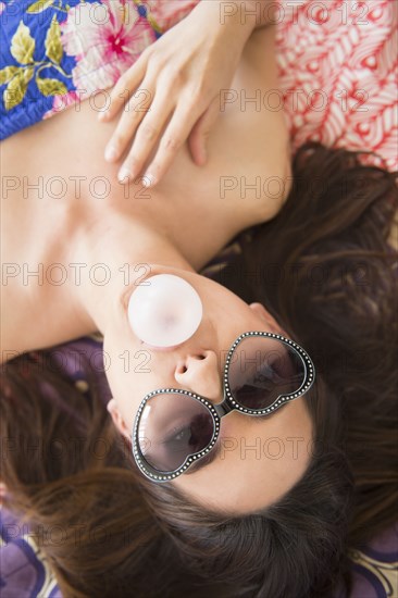 Woman in sunglasses blowing bubble gum bubble on rug