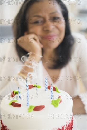 Mixed race woman blowing out birthday candles on cake
