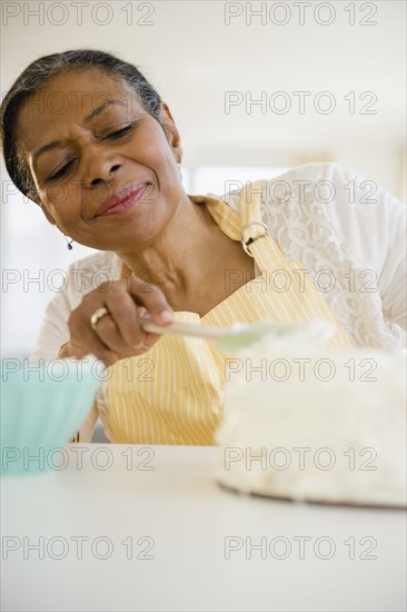 Mixed race woman frosting cake in kitchen