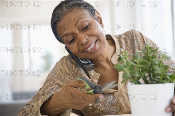 Mixed race woman trimming plant and talking on phone