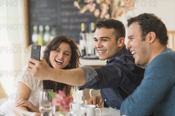 Hispanic friends taking pictures with cell phone in cafe