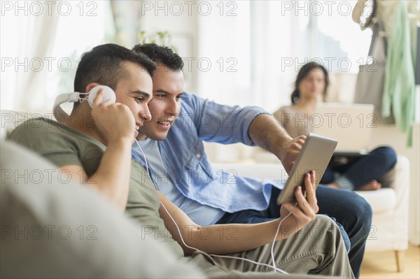 Hispanic friends using tablet computer on sofa