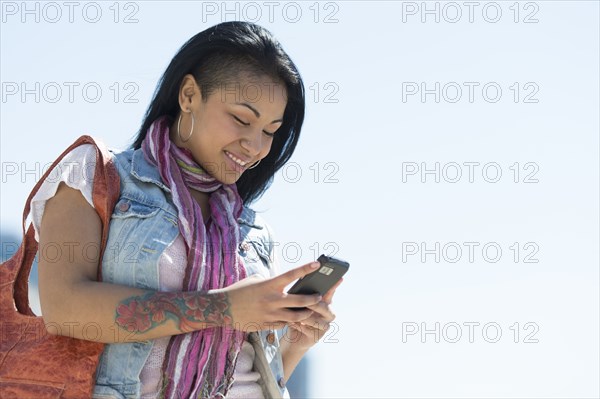 Mixed race woman using cell phone under blue sky