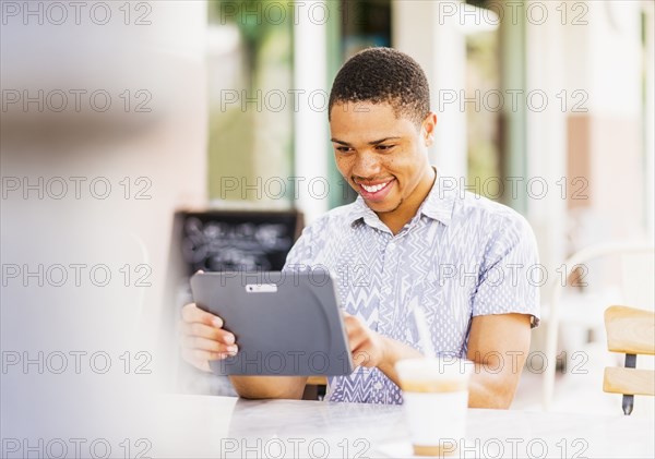 African American man using tablet computer at sidewalk cafe