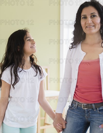 Hispanic mother and daughter holding hands in living room