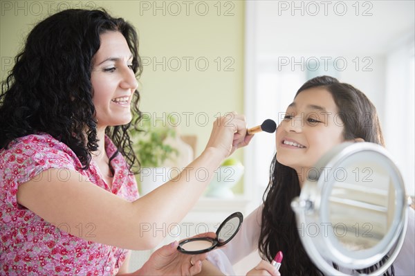 Hispanic mother helping daughter apply makeup