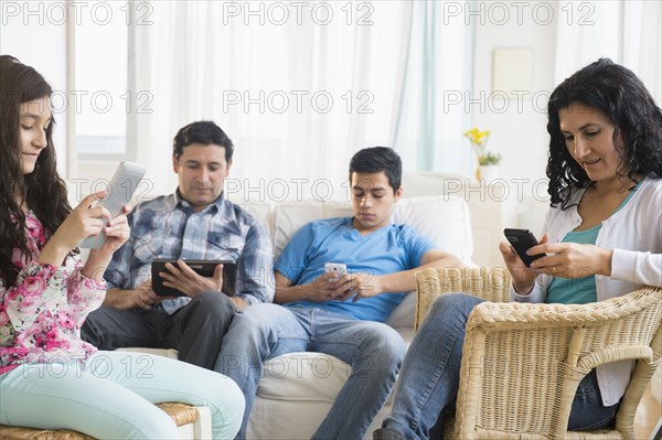 Hispanic family using cell phones and digital tablets in living room