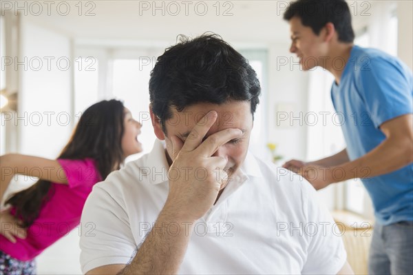 Hispanic father covering his face as children fight behind him