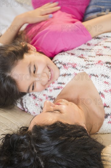 Hispanic mother and daughter relaxing together on bed