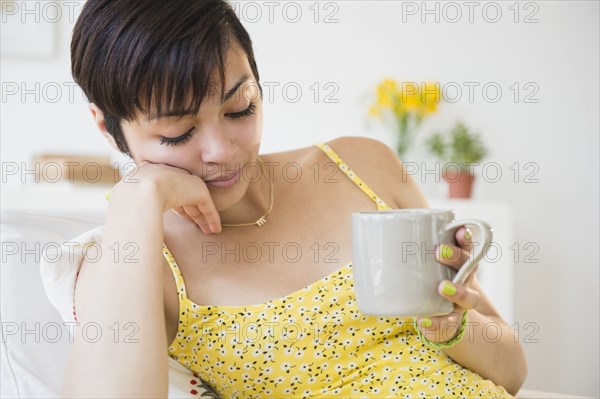 Fatigued mixed race woman drinking cup of coffee