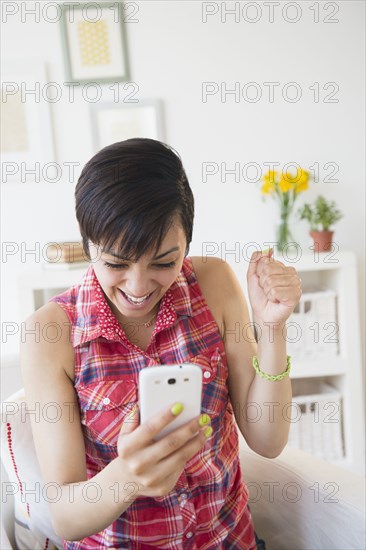 Happy mixed race woman cheering with cell phone