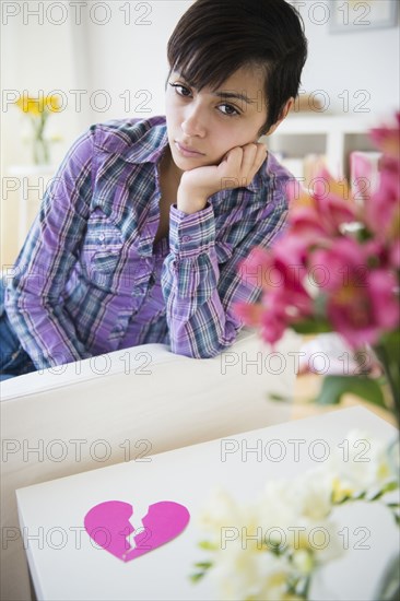 Sad mixed race woman on sofa with broken heart