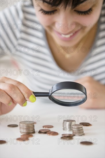 Mixed race woman examining stacks of coins with magnifying glass