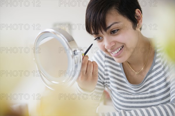 Mixed race woman applying makeup in mirror