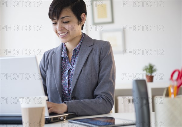 Mixed race businesswoman working on laptop computer at office desk