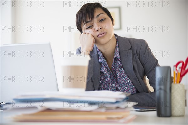 Bored mixed race businesswoman sitting at office desk