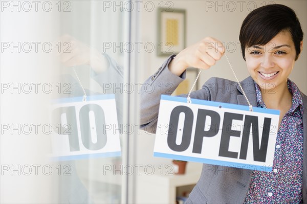 Mixed race businesswoman holding open sign