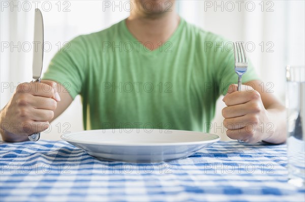 Mixed race man holding fork and knife at table