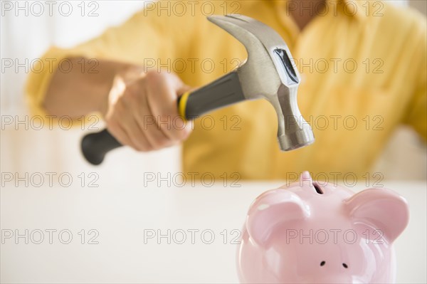 Close up of mixed race man holding hammer over piggy bank