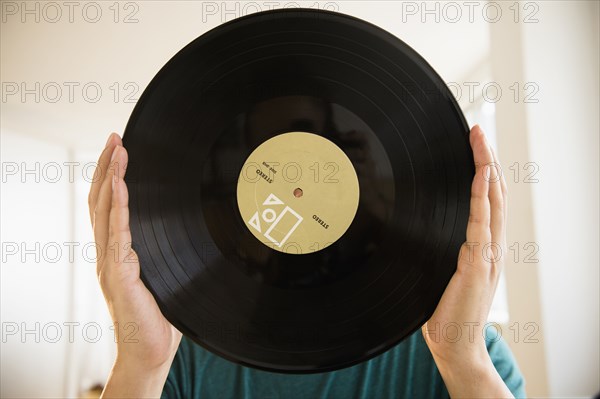 Mixed race man obscuring face with vinyl record