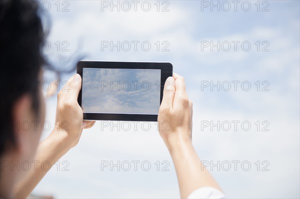 Close up of mixed race man photographing clouds with digital tablet