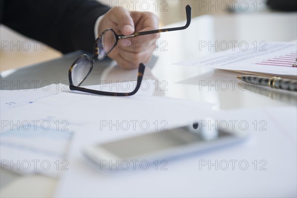 Close up of mixed race businessman holding eyeglasses at desk