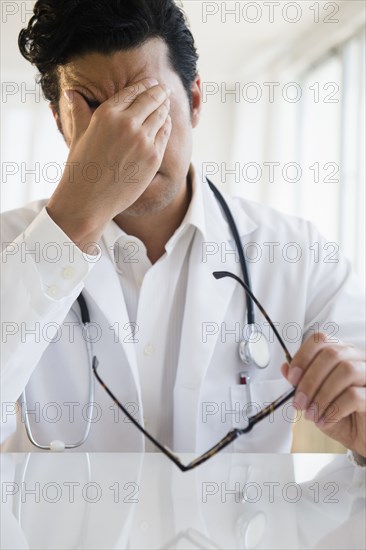 Close up of upset mixed race doctor rubbing his forehead