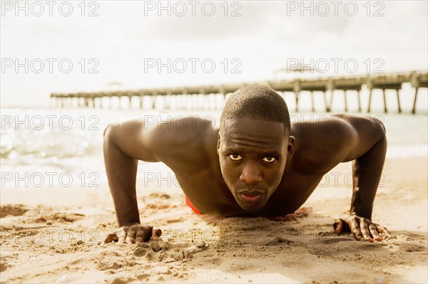 Mixed race man doing push ups on beach