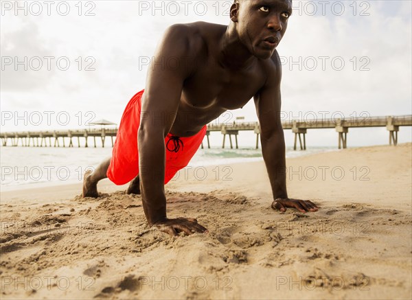 Mixed race man doing push ups on beach