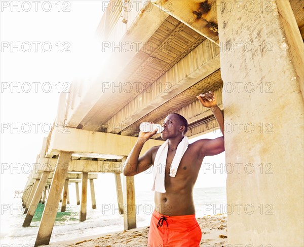 Mixed race man drinking water under pier