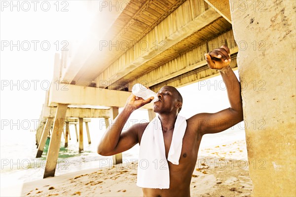 Mixed race man drinking water under pier