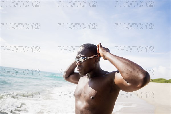 Mixed race swimmer putting on goggles at beach